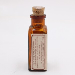 May include: A small, amber-colored glass bottle with a cork stopper. A rectangular label is affixed to the bottle, with text that reads "The word EMPLET designates the enteric coated tablets manufactured by Parke, Davis & Co."