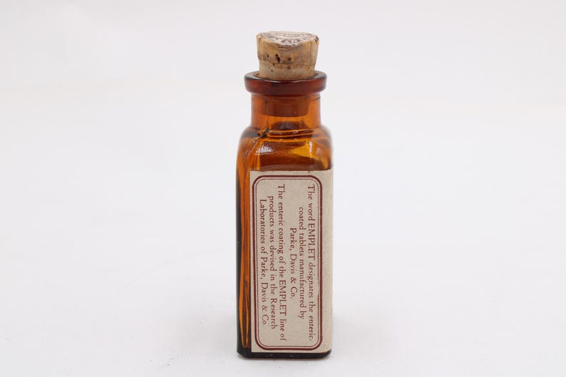 May include: A small, amber-colored glass bottle with a cork stopper. A rectangular label is affixed to the bottle, with text that reads "The word EMPLET designates the enteric coated tablets manufactured by Parke, Davis & Co."
