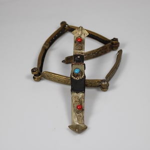 May include: An antique metal object with a central, decorated section and curved arms. The central piece features red and turquoise accents. The object has a vintage, possibly handcrafted appearance.