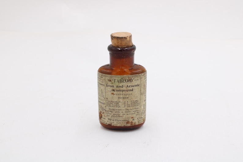 May include: A small, antique brown glass bottle with a cork stopper. The label reads "TABLOID" Iron and Arsenic Compound, with additional text detailing the contents and usage. The bottle is likely from the early 20th century.