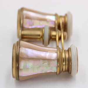 May include: Antique opera glasses with a gold-tone metal frame and iridescent mother-of-pearl inlay. The lenses are white, and the binoculars are connected by a gold-tone bridge. A classic accessory.