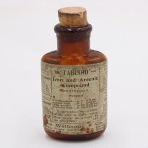 May include: A small, antique brown glass bottle with a cork stopper. The label reads "TABLOID" and "Iron and Arsenic Compound, Compressed Poison." The bottle has a vintage aesthetic, with faded text and a classic design.