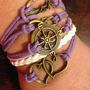 May include: A purple and white braided bracelet with a compass, anchor, and double heart charms.