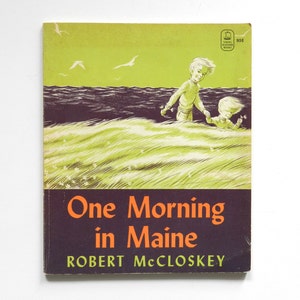 May include: A vintage children's book titled One Morning in Maine by Robert McCloskey. The cover features a green and dark brown illustration of two children walking through tall grass near the ocean with seagulls flying in the sky above.
