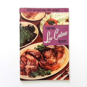 May include: A vintage cookbook titled Tempting Low-Calorie Recipes with the subtitle 253 eat-and-stay-thin recipes. The cover features a colour photograph of a cooked meat dish on a platter, a green gelatin mould, and a salad with tomatoes.