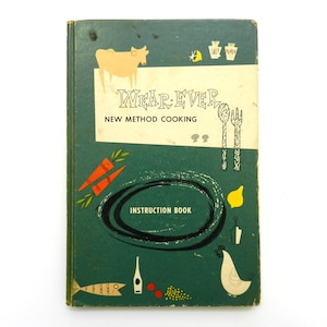 May include: A dark green vintage instruction book titled Wear-Ever New Method Cooking. The cover features mid-century style illustrations of a cow, carrots, a fish, a chicken, a lemon, and kitchen utensils in orange, yellow, and white ink.