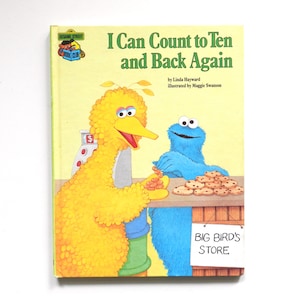 May include: A yellow hardback children's book titled I Can Count to Ten and Back Again. The cover features Big Bird and Cookie Monster at a counter with cookies and a cash register. A sign on the counter reads Big Bird's Store.