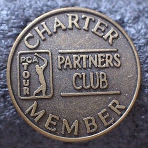 May include: A bronze-colored metal token with the text "Charter Partners Club Member" and a logo of a golfer with the text "PCA Tour".