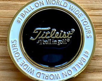 Peut inclure: Un marqueur de balle de golf de couleur or avec une bordure blanche. Le marqueur présente le texte "#1 BALL ON WORLD WIDE TOURS" et le logo Titleist avec le texte "#1 ball in golf®".