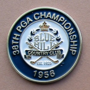 Könnte beinhalten: Eine blaue und goldene Metallnadel zur Erinnerung an die 38. PGA Championship, die 1956 im Blue Hill Country Club ausgetragen wurde. Die Nadel zeigt das Logo des Clubs mit einer Krone, gekreuzten Golfschlägern und dem Text "Blue Hill Country Club Est. 1925".
