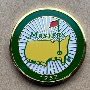 Può includere: Un segnapallina da golf rotondo con bordo dorato e bordo verde. Il centro presenta una mappa gialla degli Stati Uniti, una bandiera rossa, la scritta "MASTERS" e l'anno "1952".