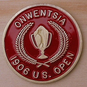 Peut inclure: Une pièce de monnaie en métal rouge et or avec le texte "ONWENTSIA 1906 U.S. OPEN" autour du bord. Un trophée en or avec un golfeur est au centre de la pièce.