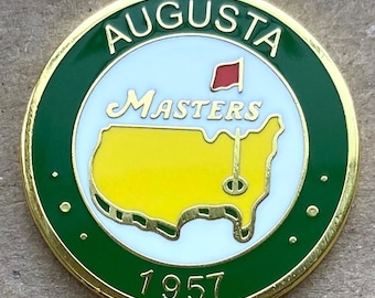 Peut inclure: Épinglette ronde à bordure dorée et bordure verte. Elle affiche le mot "AUGUSTA" et "MASTERS" avec un drapeau rouge et une carte jaune des États-Unis avec un drapeau de golf. L'année "1957" est inscrite en bas.