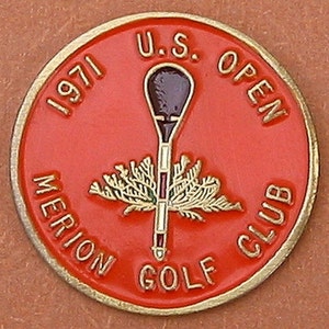 Könnte beinhalten: Ein roter und goldener Golfball-Marker mit dem Text "1971 U.S. OPEN MERION GOLF CLUB". Der Marker zeigt einen stilisierten Golfschläger und einen grünen Baum.