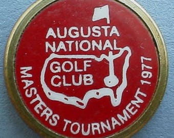 Könnte beinhalten: Ein rot-weißer Golfball-Marker mit dem Text "Augusta National Golf Club Masters Tournament 1977". Der Marker zeigt eine weiße Umrandung der Vereinigten Staaten mit einem Golfplatz im Inneren.