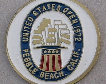 Peut inclure: Une pièce de monnaie dorée avec un fond blanc et un cercle bleu et or au centre. Le cercle contient un graphique d'un sac de golf avec des clubs et un chapeau avec des étoiles et des rayures. Le texte autour du cercle indique "United States Open 1972 Pebble Beach Calif."