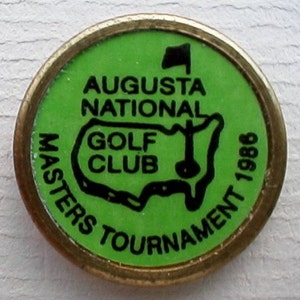May include: A green and gold golf tournament pin with the text "Augusta National Golf Club Masters Tournament 1988" and a black outline of the United States.