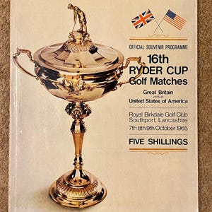 Op de afbeelding: Een vintage souvenirprogrammacover met een gouden Ryder Cup-trofee en een golferfiguur. De cover toont de vlaggen van Groot-Brittannië en de Verenigde Staten, en tekst die de 16e Ryder Cup Golf Matches aangeeft.