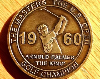 May include: A bronze golf champion medal commemorating Arnold Palmer's 1960 wins at The Masters and The U.S. Open. The medal features a profile image of Palmer swinging a golf club, with the text "The Masters The U.S. Open 1960 Arnold Palmer 'The King' Golf Champion" around the edge.