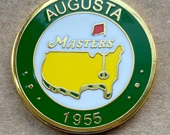 Peut inclure: Épinglette ronde à bordure dorée et verte, avec le mot "AUGUSTA" en blanc. Le centre présente un cercle blanc avec "Masters" et une carte jaune des États-Unis. Un drapeau rouge et l'année "1955" sont également visibles.