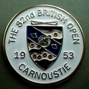 May include: A white metal pin with a gold rim. The pin features a crest with a blue and white shield, red dots, and a white banner. The text "THE 82nd BRITISH OPEN 1953 CARNOUSTIE" is printed around the crest.