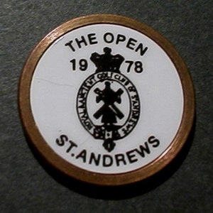 May include: A white and gold round coin with the text "The Open 1978" and "St. Andrews" around a black and white crest with a crown.