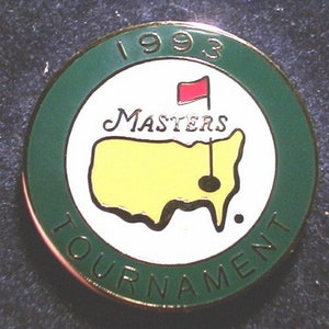 May include: A green and white golf ball marker with the text "1993 Masters Tournament" and a yellow outline of the United States with a red flag and a black golf hole.