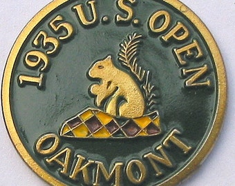 Peut inclure: Épingle de golf vintage avec un écureuil doré sur une plateforme à carreaux, avec le texte "1935 U.S. OPEN OAKMONT" en lettres dorées sur fond vert. L'épingle a une bordure dorée.