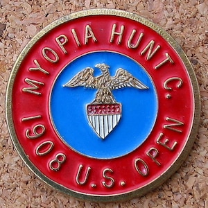 Może przedstawiać: Okrągła, czerwono-złota odznaka z napisem "MYOPIA HUNT C. 1908 U.S. OPEN" wokół krawędzi. W środku znajduje się niebieski okrąg z złotym orłem trzymającym tarczę z czerwonymi i białymi paskami.