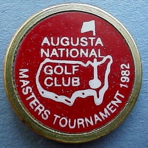 Può includere: Un segnalibro per palline da golf rosso e bianco con il testo "Augusta National Golf Club Masters Tournament 1982" e un contorno bianco degli Stati Uniti.