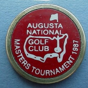 Könnte beinhalten: Ein roter und weißer Golfball-Marker mit dem Text "Augusta National Golf Club Masters Tournament 1987" und einer weißen Umrandung der Vereinigten Staaten mit einem Golfloch und einer Fahne.