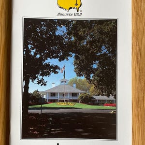 May include: A white pamphlet with a yellow and red logo for the Masters Tournament at Augusta National Golf Club in Augusta, Georgia, USA. The pamphlet features a photo of the clubhouse and the text "strokesaver THE WORLD'S NO 1 GOLF COURSE GUIDE TM".