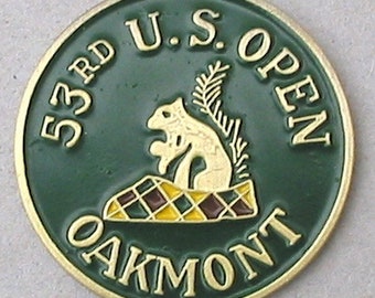 Puede incluir: Un marcador de bola de golf verde y dorado con el texto "53rd U.S. OPEN OAKMONT" y una ardilla sentada sobre un patrón a cuadros.