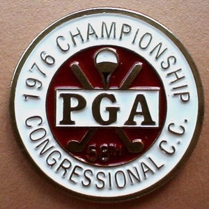 以下が含まれることがあります： 「1976 PGA Championship Congressional C.C. 58th」という文字と、交差したゴルフクラブとゴルフボールが描かれた赤と金のロゴがついた、白と金の円形のピンバッジです。