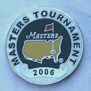 May include: A circular Masters Tournament commemorative coin from 2006. The coin features the words "MASTERS TOURNAMENT" in a white font around the edge. The centre has a green background with a gold outline of the United States, a red flag, and the word "MASTERS".