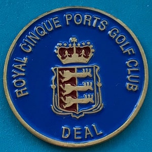 Pode incluir: Um alfinete de clube de golfe dourado e azul com o texto "Royal Cinque Ports Golf Club Deal" e um brasão com uma coroa.