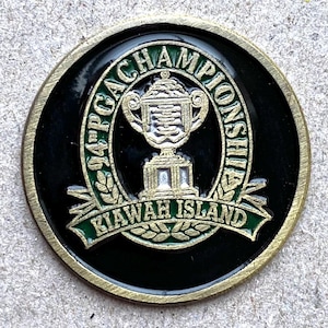 Op de afbeelding: Een ronde, zwart-gouden golf toernooimunt. De munt toont de tekst "94 PGA Championship" en "Kawah Island" in groene letters. Een gouden trofee staat in het midden.