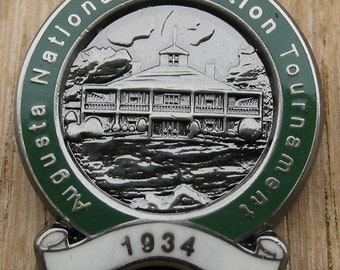Könnte beinhalten: Eine grüne und weiße Emaille-Anstecknadel mit einem silbernen Bild eines Gebäudes und dem Text "Augusta National Invitation Tournament 1934".