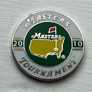 Peut inclure: Un marqueur de balle de golf du tournoi Masters blanc, argenté et vert avec le texte "Masters Tournament" et "2010" imprimé dessus.