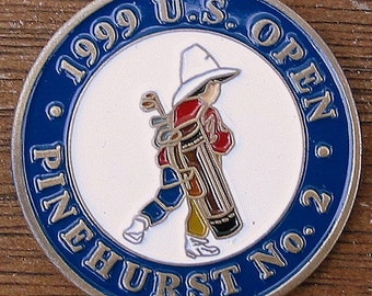 May include: A blue and silver commemorative coin with the text "1999 U.S. OPEN PINEHURST No. 2" around the edge. In the centre is a cartoon golfer wearing a white cowboy hat and carrying a golf bag.