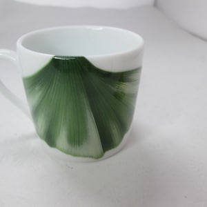 May include: White ceramic teacup with a green ginkgo leaf design.