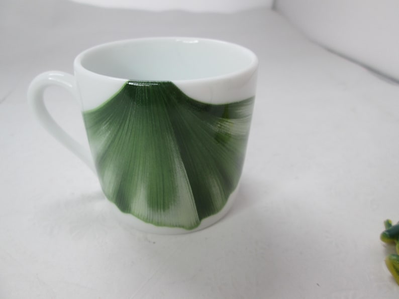 May include: White ceramic teacup with a green ginkgo leaf design.