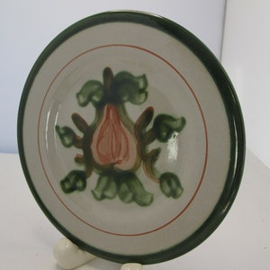 May include: A white ceramic plate with a green rim and a hand-painted design of a pink pear with green leaves.