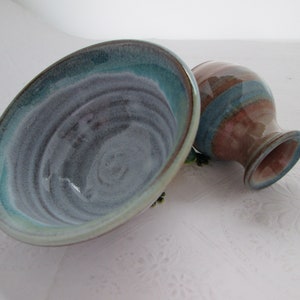 May include: A set of two handmade ceramic bowls, one a larger bowl with a light blue and gray glaze, and the other a smaller bowl with a pink and blue glaze.