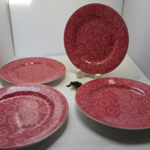 May include: Four pink dinner plates with a swirl pattern. The plates are made of ceramic and have a glossy finish.