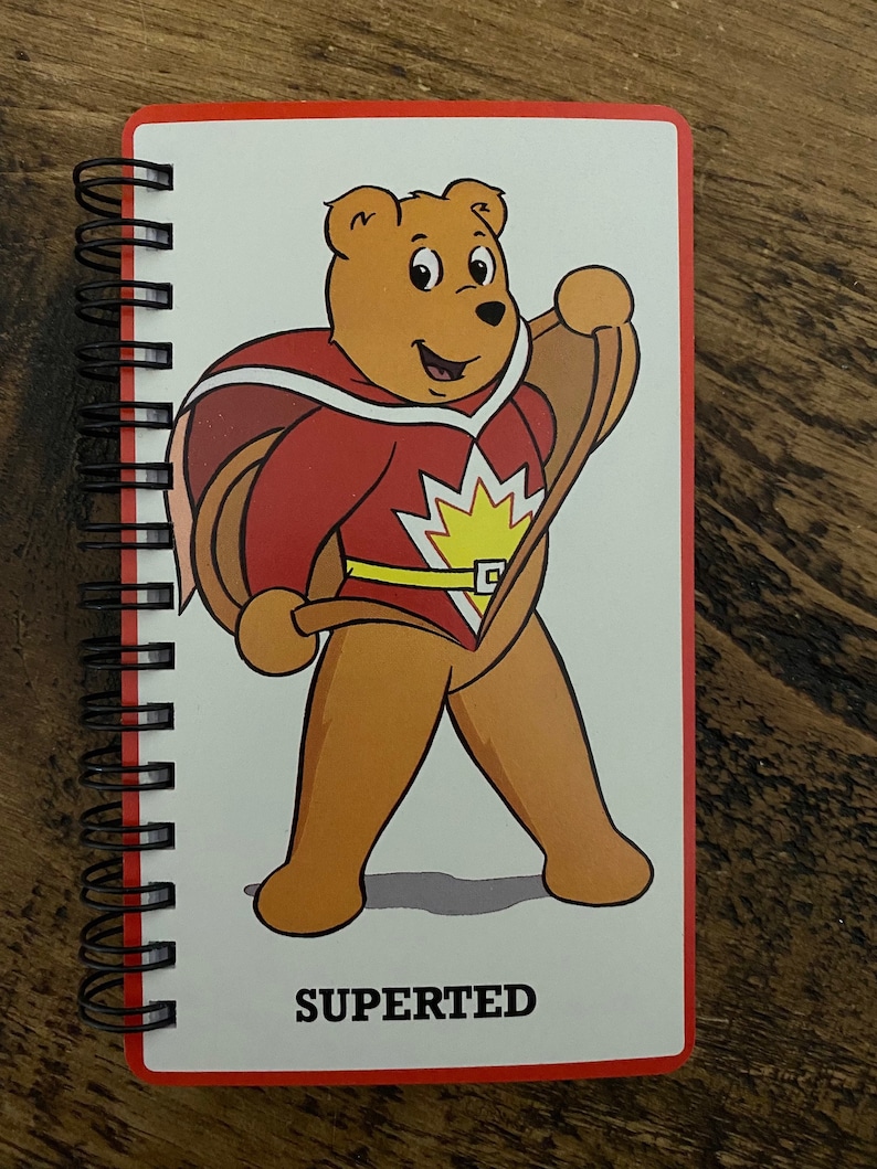 May include: A red and yellow superhero bear with a cape and a belt, standing with a smile. The text "SUPERTERD" is printed below the bear.