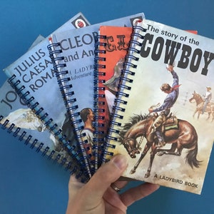 May include: A collection of five small, spiral-bound Ladybird books with colourful covers. The books are titled "Julius Caesar and the Roman", "Cleopatra and Antony", "The Story of the Cowboy", and two others with titles that are partially obscured.