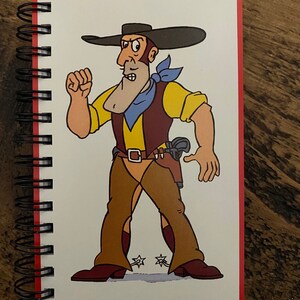 May include: A red spiral bound notebook with a cartoon illustration of a cowboy wearing a brown hat, yellow shirt, blue bandana, and brown pants with spurs. The cowboy is holding a gun and has a stern expression. The text "TEXAS PETE" is printed below the illustration.