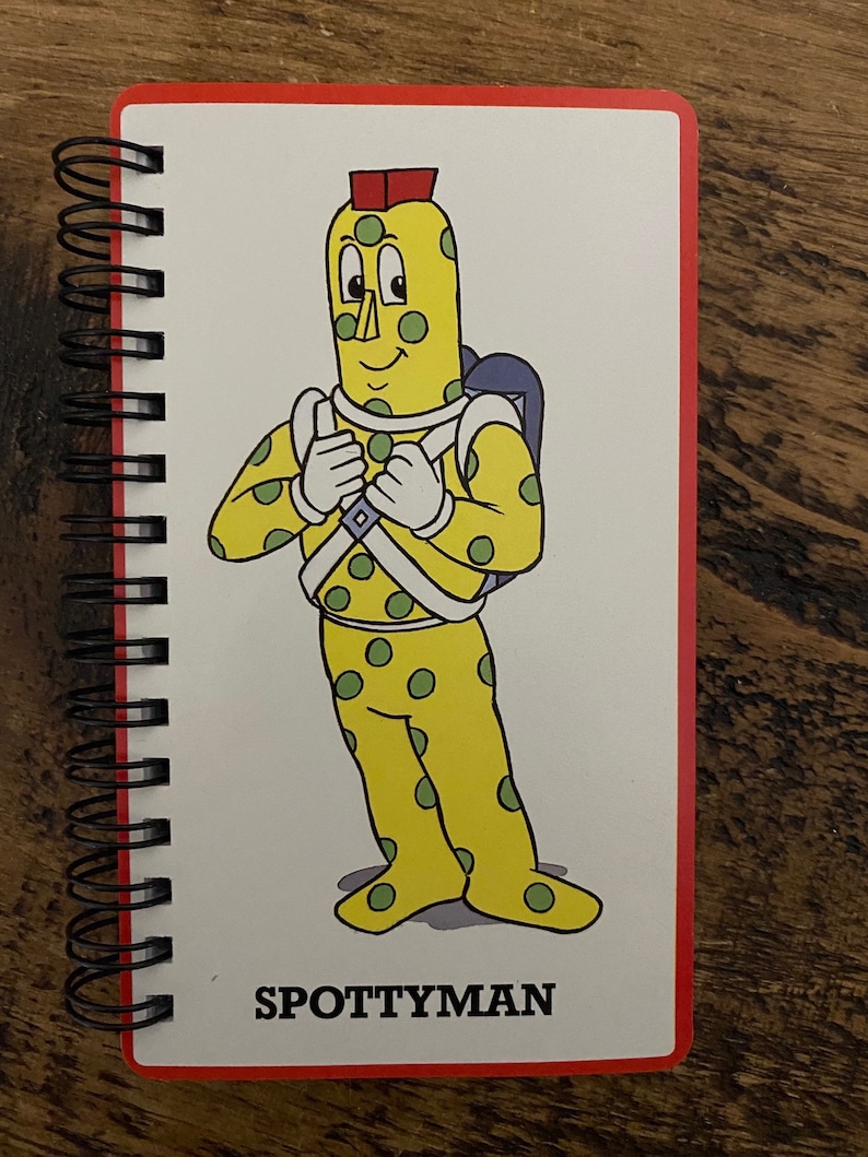 May include: A yellow character with green spots and a red hat, wearing a white and green suit. The character is standing with arms crossed and the text "SPOTTYMAN" is below the character.