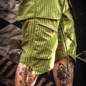 May include: Green striped cargo shorts with a black belt and a zippered pocket. The shorts have a relaxed fit and are made of a lightweight fabric.
